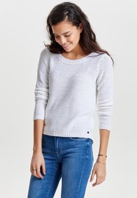 Maglione grigio chiaro in maglia con scollo rotondo, maniche lunghe, bordo a costine e motivo lavorato a trama. Abbinato a jeans blu.