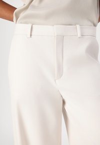 Witte, op maat gemaakte broek met een gladde textuur, vlakke voorkant, zijzakken en riemlussen. Kenmerkt zich door een schone, minimalistische stijl zonder patronen.