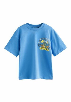Vaaleansininen puuvillapaita, jossa on pyöreä kaula-aukko ja lyhyet hihat. Tässä on värikäs "SURFOSAURUS" -grafiikka, jossa on sarjakuvamainen dinosaurus ja auringon kuva.
