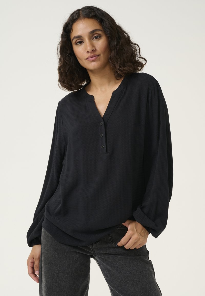 Blouse noire à manches longues en tissu texturé avec un col henley et trois boutons, présentant des manches froncées et une coupe décontractée.