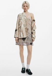Beige lagerklädsel med en tryckt jacka och en klänning med olika grafiska mönster. Innehåller en genomskinlig textur, med rak skärning och avslappnade sneakers.