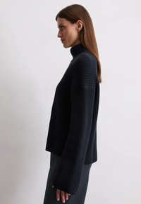 Navy turtleneck sweater in textured knit, featuring wide sleeves and a relaxed fit, with a high collar and ribbed details.