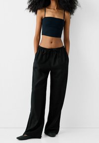 Crop top noir avec des fines bretelles associé à un pantalon noir ample avec une taille élastique et des poches latérales, porté avec des chaussures slip-on texturées.
