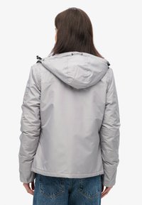 Grå isoleret jakke med hætte, der har elastiske manchetter og snoretræk. Glat tekstur med en let skinnende finish. Casual design.