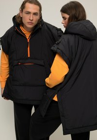 Gilet imbottiti neri con accenti arancioni, dotati di un alto colletto, tasca frontale e maniche corte. Tessuto liscio, design sportivo.