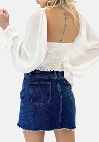 Weißes Langarmbluse mit puffigen Ärmeln und gerafftem Taillenbund; kombiniert mit einem dunkelblauen Denim-Minirock mit fransigem Saum und Taschen.