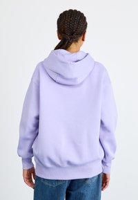 Sweatshirt lilás com um capuz grande, punhos e cintura canalçados. Feito de um material suave, apresenta um corte descontraído e um design simples.