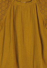 Blusa gialla senape con un corpo testurizzato e un intricato design a occhiello lungo le spalle, con scollatura arricciata e un tessuto leggero.