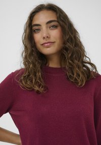 Burgundská pletená mikina s klasickým výstrihom, ktorá sa vyznačuje jemnou textúrou a jemným leskom, s krátkymi rukávmi a voľným strihom.