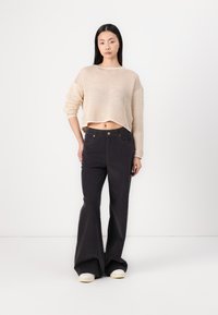 Beige knitted cropped sweater with wide sleeves paired with high-waisted black flared pants. Shoes are light with a textured upper.