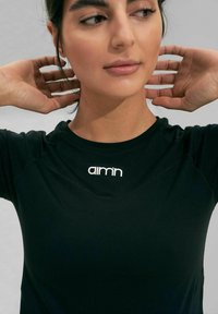 T-shirt de sport noir avec un col rond, arborant un logo blanc sur la poitrine. Texture lisse et coupe ajustée.