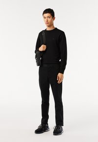 Felpa nera e pantaloni, design minimale. Sneakers nere con suola testurizzata. Piccola borsa appesa alla spalla.