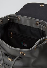 Sac en cuir synthétique gris avec doublure en tissu. Garnitures en métal doré, fermeture à cordon de serrage et poche intérieure zippée. Étiquette de la marque visible.