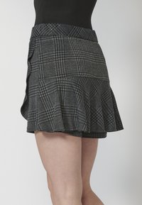 Falda corta de cuadros grises con un dobladillo acampanado, que presenta una cintura ajustada y un tejido texturizado. Contiene un patrón de cuadros sutil.