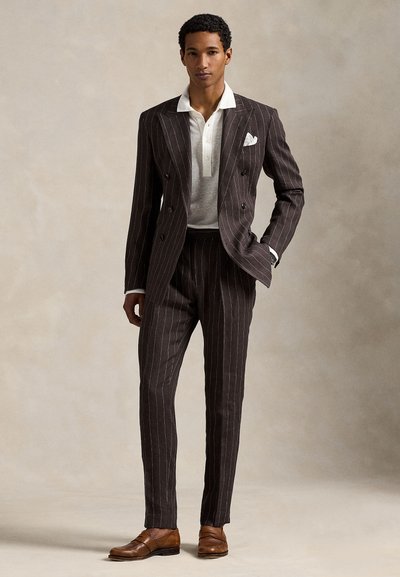Σκούρο κοστούμι με λεπτές ρίγες, διπλό στήθος και εφαρμοστή γραμμή, συνδυασμένο με ανοιχτό πουκάμισο πόλο. Ανοιχτά καφέ δερμάτινα παπούτσια.