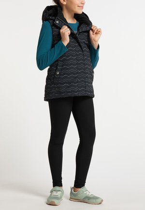 Musta pehmeä liivi, jossa on viistokuvio, varustettuna hupulla, etupainikkeilla ja sivutaskuilla. Yhdistetty siniseen pitkähihaiseen paitaan ja mustiin legginseihin.