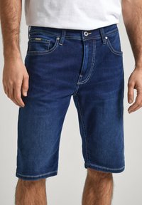 Pantalones cortos de mezclilla en azul oscuro con corte recto y diseño de cinco bolsillos. Presenta costuras de contraste y cierre de botón.
