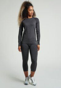 Langärmliges, dunkelgraues Sportshirt mit strukturierten Akzenten an den Schultern, kombiniert mit passenden Capri-Leggings und hellgrauen Sneakers.