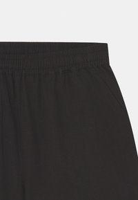 Calças pretas de cintura elástica com uma textura suave, apresentando bolsos laterais e um corte relaxado. O tecido é leve e respirável.