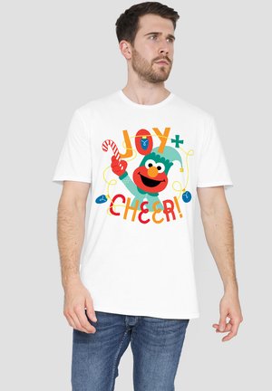 White cotton t-shirt featuring a colorful Elmo graphic with text "JOY+" and "CHEER!" along with a candy cane and decorative elements.