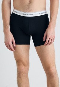 Boxer da uomo in cotone nero con una fascia in vita elastica bianca con il branding "Calvin Klein". Design aderente con una texture liscia.