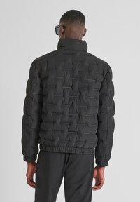 Crna puffer jakna s kvadratnim uzorkom, visokim ovratnikom i elastičnim manžetama. Materijal izgleda glatko i podstavljen je za toplinu.