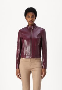 Giacca in pelle bordeaux con colletto alto, chiusura con zip e tasche laterali. Presenta un design aderente e dettagli di cucitura sottili.