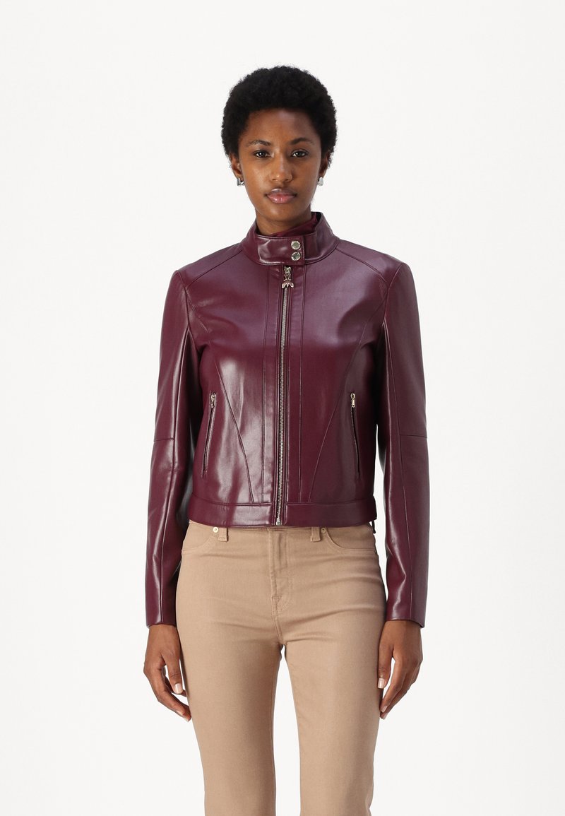 Giacca in pelle bordeaux con colletto alto, chiusura con zip e tasche laterali. Presenta un design aderente e dettagli di cucitura sottili.