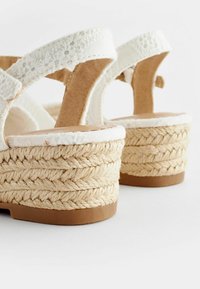 Zeppe espadrille bianche con dettagli in corda di juta, morbidi cinturini in tessuto e suola in gomma color sabbia. Presentano una cucitura floreale sui cinturini.