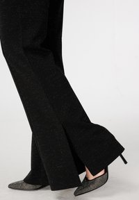 Zwarte uitlopende broek met een subtiele glinsterende textuur. Gecombineerd met zwarte puntige schoenen met een diamantachtige versiering op de neus.