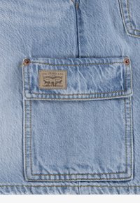 Poche de veste en jean bleu clair avec étiquette marron Levi Strauss & Co. et coutures jaunes visibles ainsi que rivets en cuivre aux coins supérieurs.