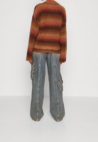 Jersey de punto de gran tamaño con cálidas rayas tonales en marrón y rojo, combinado con pantalones cargo de mezclilla de pierna ancha con bolsillos laterales.