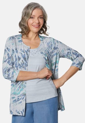Leichtes, offenes Cardigan in blau-weißer abstrakter Druck, mit 3/4-Ärmeln, kombiniert mit einem leichten gestreiften Tanktop und blauen Hosen.