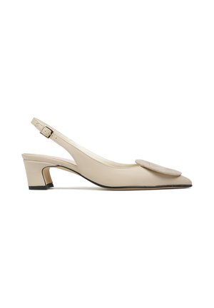 Beżowy skórzany but na niskim obcasie typu slingback, ze spiczastym noskiem i dużą okrągłą dekoracyjną aplikacją na wierzchu.