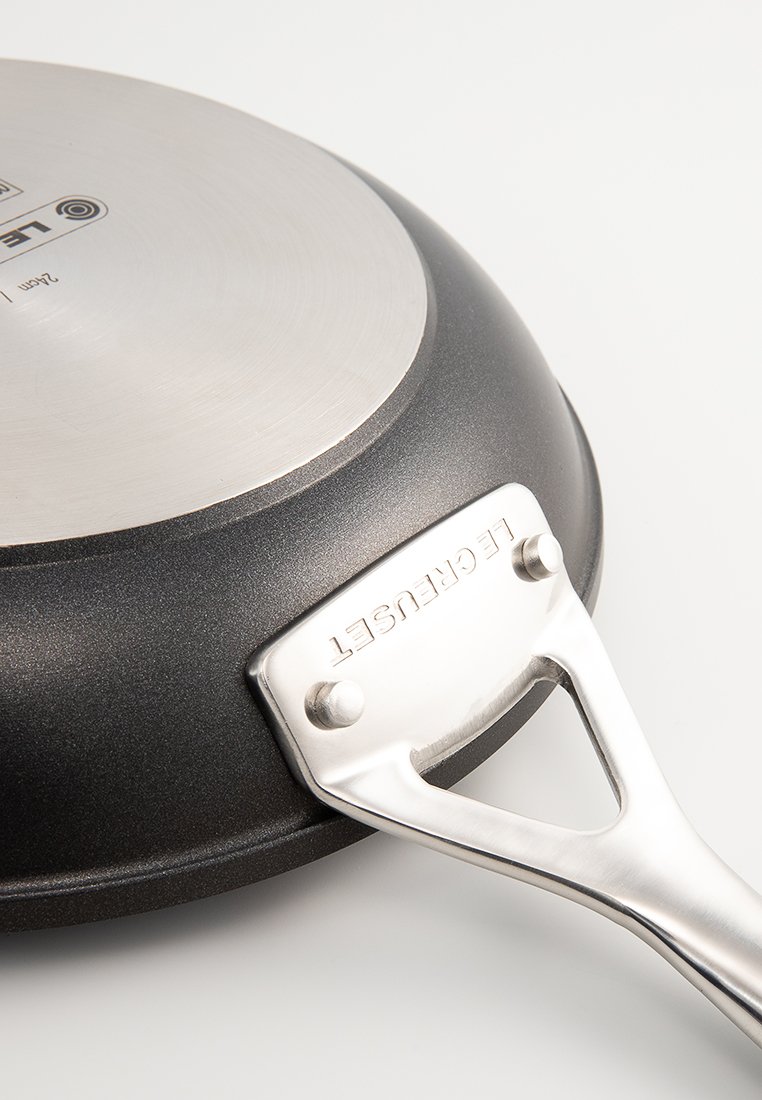 Czarna patelnia teflonowa z uchwytem ze stali nierdzewnej i gładką metaliczną powierzchnią, z delikatnym zakrzywieniem i logo na podstawie.