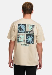 Beige short-sleeve t-shirt featuring a multi-panel graphic print on the back in blue and black with the "Billabong" logo at the bottom.