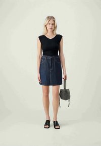 Black fitted t-shirt paired with a dark denim A-line skirt, worn with black slide sandals; model holding a small, patterned handbag.