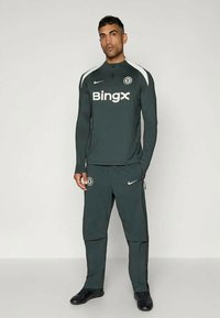 Urheiluasu tummanharmaana. Sisältää pitkät hihat, pyöreän kaula-aukon, Niken logon ja Bingx-tekstin. Housuissa on sivutaskut ja Chelsea-embleemi.