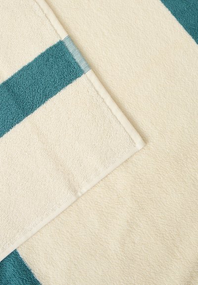 Gros plan d'une serviette crème pliée avec une bande verte, montrant une texture douce et des bords cousus propres.