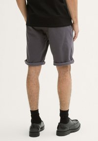 Pantalones cortos grises con puños enrollados, hechos de una tela ligera, combinados con calcetas y zapatos negros, mostrando una vista trasera casual.