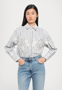 Λευκό και γκρι ριγέ πουκάμισο με κεντημένα λουλούδια, μακριά μανίκια και κλασικό γιακά, συνδυασμένο με ψηλόμεσα μπλε τζιν.