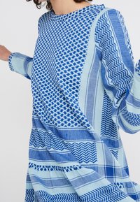 Sininen kuvioitu pitkähihaine paita, jossa on erilaisia geometrisia muotoja sinisen ja vaaleansinisen sävyissä. Rentoa istuvuutta ja pyöreä pääntie.