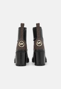 Zwarte en bruine enkellaarsjes met een chunkyzool, voorzien van een logo-accent en een gestructureerde stof in een monogrampatroon aan de achterkant.