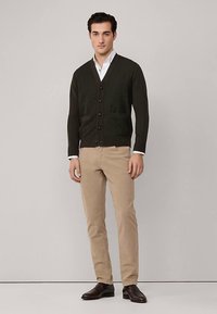 Mörkgrön stickad kofta med V-ringning, knappar fram och två fickor, kombinerad med beige byxor och bruna läderskor.