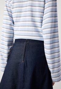 Lys blåstripet langermet topp kombinert med et mørkt denimskjørt med søm bak og subtil sømdetalj.