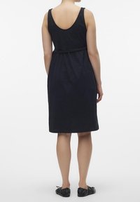 Svart ärmlös klänning med rund rygg, figurnära midja och knälång nederkant. Mjuk textur, minimal design, inga synliga mönster eller metallringar.