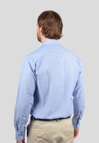 Camicia a maniche lunghe azzurro chiaro con colletto formale, texture liscia, polsini abbottonati e dettaglio sullo yoke posteriore. Abbinata a pantaloni beige.