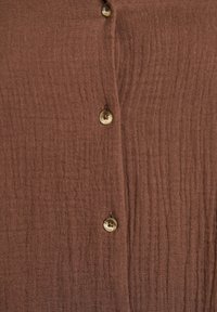 Brown button-up shirt with a textured, crinkled fabric and two buttons at the front, featuring a subtle, natural sheen.