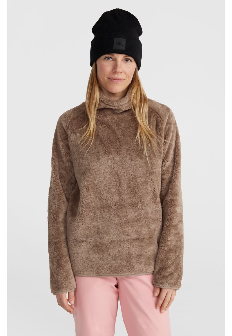 Bruine fleece pullover met een hoge kraag, gestructureerd oppervlak en lange mouwen, gecombineerd met een zwarte gebreide beanie. Roze broek is zichtbaar.
