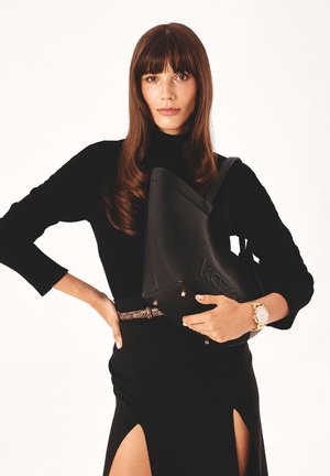 Must have must be tan leather handbag with structured shape, engraved logo and gold hardware, held by a person wearing a black top and skirt with a side slit.